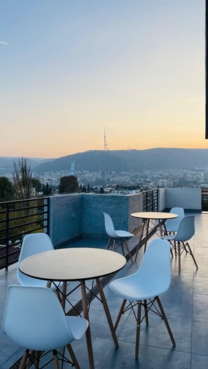 A rooftop terrace with white chairs and tables, offering a view of a cityscape and a distant tower. - Ncomforts Stay inn (Tbilisi)
