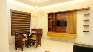 A modern living room with a dining area, a flat-screen TV mounted on a wooden wall, and a black sofa. - Ncomforts Stay inn (Tbilisi)