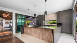 A modern kitchen with a wooden island, pendant lights, and a view of the outdoors. - Tranquil Beach Side Retreat - Inquire 4 Long Stay Discounts (Mount Coolum)