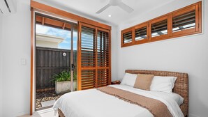 A bedroom with a bed, wooden shutters, a ceiling fan, and a view through a sliding door to an outdoor area. - Tranquil Beach Side Retreat - Inquire 4 Long Stay Discounts (Mount Coolum)
