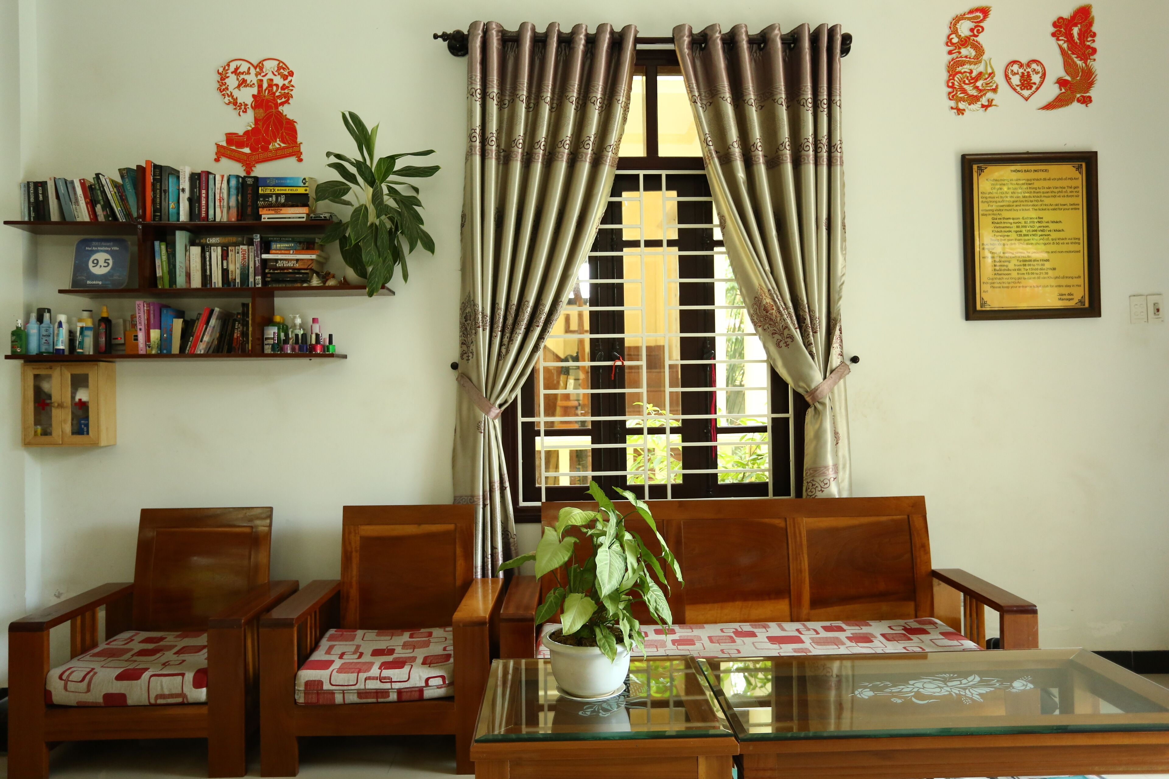 A living room with a sofa set, a glass coffee table, a bookshelf, and a window with curtains.