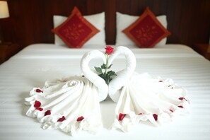 Un letto rifatto con cura, decorato con un asciugamano a forma di cuore e una rosa.