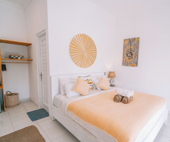 A bedroom with a bed, a bedside table with a lamp, a wall art piece, and a shelf with decorative items.
