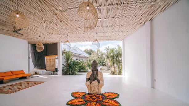Ein Zimmer mit einer großen Buddha-Statue, einer gewebten Decke und einem modernen Sofa.