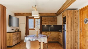 Una cocina compacta con armarios de madera, una mesa de comedor con sillas, un televisor montado en la pared y un ventanal que proporciona luz natural.