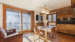 Una cocina moderna con armarios de madera y una estufa integrada. Hay una mesa de comedor con sillas y un televisor montado en la pared.