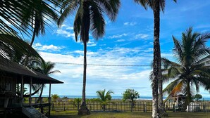 Una propiedad frente a la playa con una estructura de madera, palmeras y un área cercada.