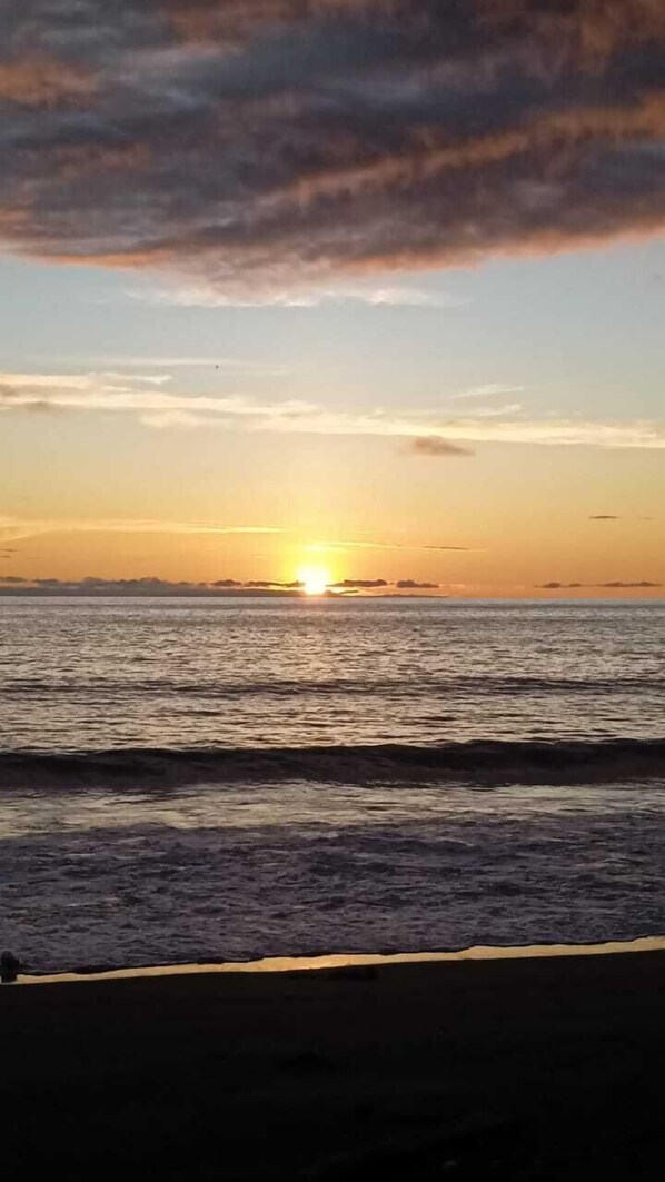 Un coucher de soleil sur une mer calme, avec une plage au premier plan.