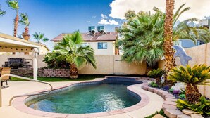 A backyard with a swimming pool, palm trees, and a stone wall. - Night at the Roxford 4b 3ba Pool (Las Vegas)