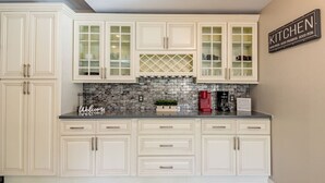 A kitchen with white cabinets, a tiled backsplash, and a coffee station. - Night at the Roxford 4b 3ba Pool (Las Vegas)