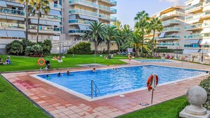 A swimming pool surrounded by a grassy area with palm trees, a lifebuoy, and a stone balustrade.