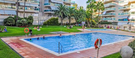 A swimming pool surrounded by a grassy area with palm trees, a lifebuoy, and a stone balustrade.
