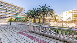 A paved walkway with a railing, palm trees, and multi-story buildings in the background.