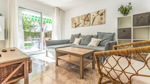 A modern living room with a grey sofa, wooden coffee table, wicker chair, and a sliding glass door leading to an outdoor area.