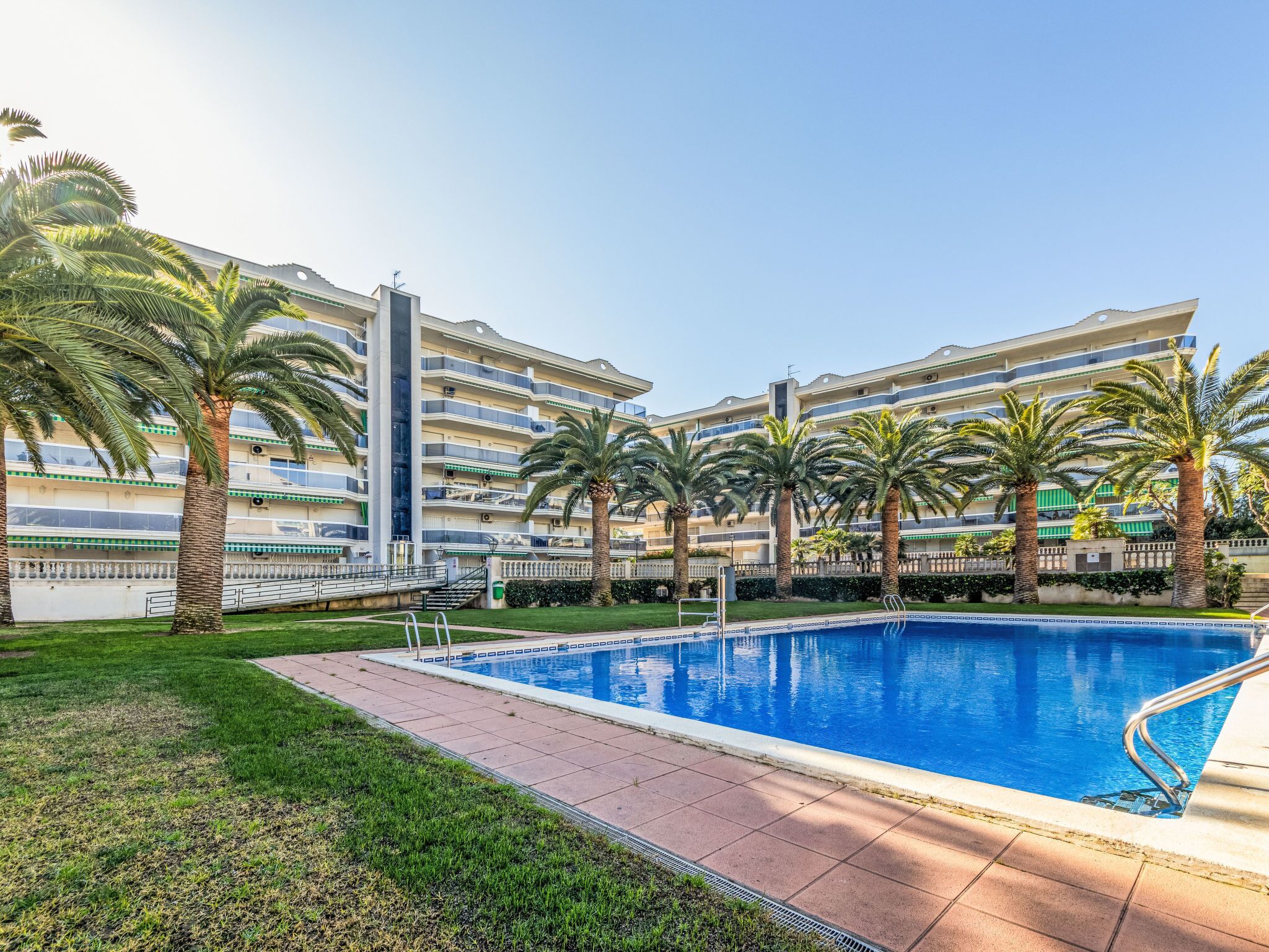 A swimming pool surrounded by palm trees and a multi-story building with balconies.