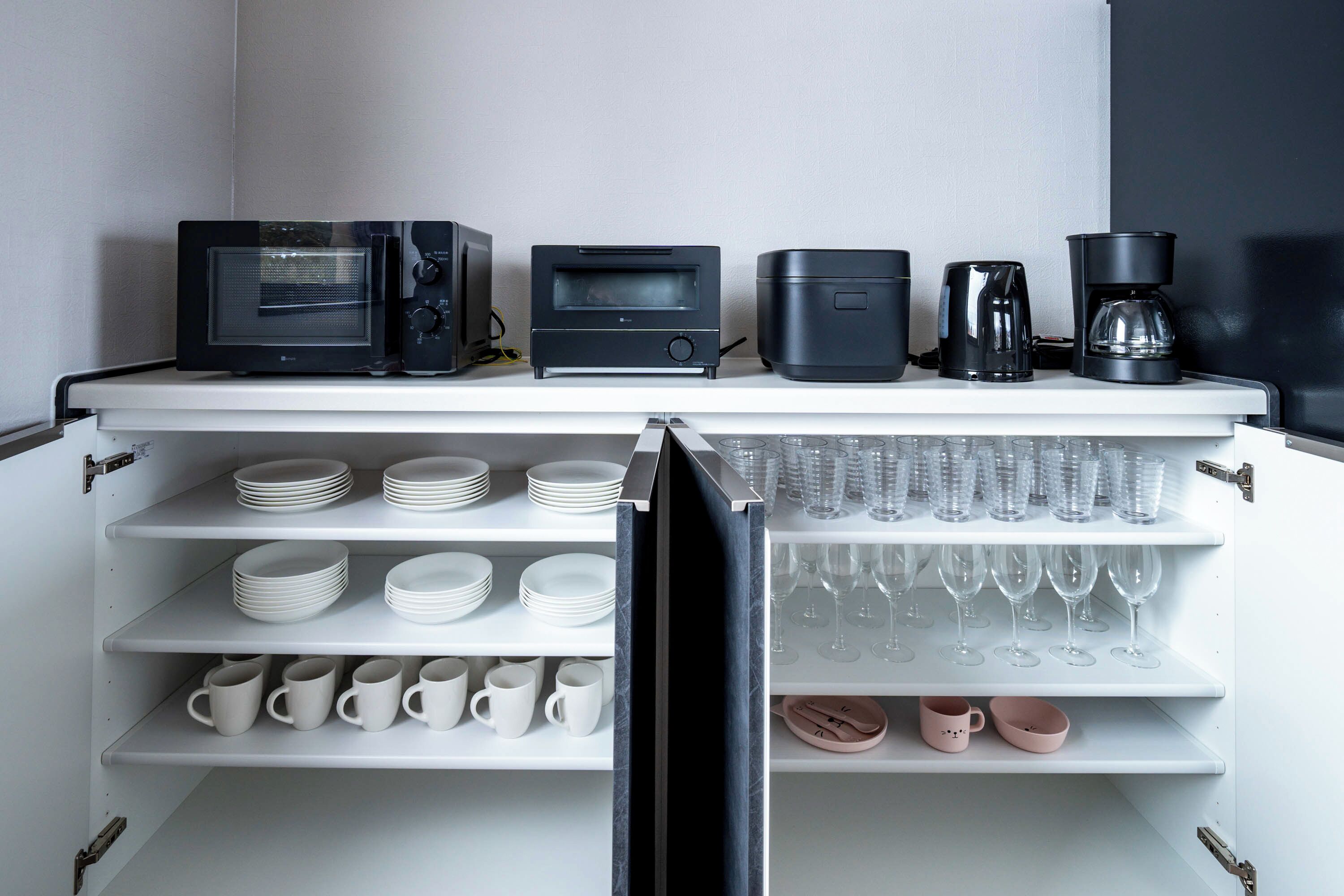 Une cuisine équipée d’un four à micro-ondes, d’un grille-pain, d’une machine à café et d’étagères contenant des assiettes, des tasses et des verres à vin.