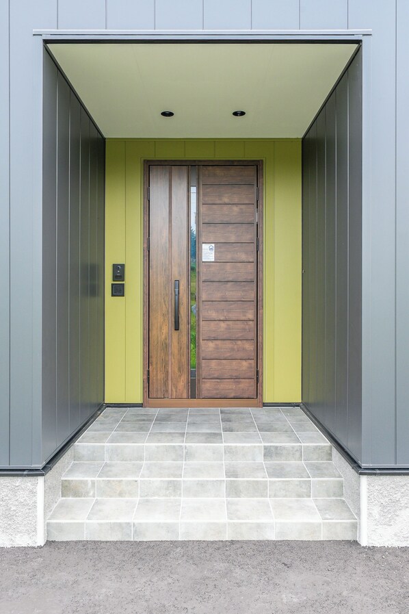 A building entrance with a wooden door, a small step leading up to it, and a light green wall.