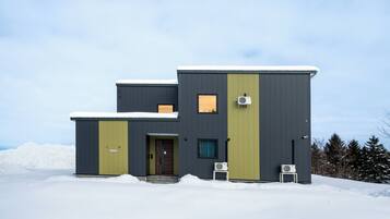 A modern two-story building with a dark exterior and a green door, surrounded by snow.