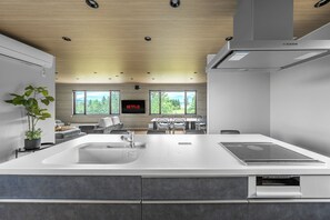 A modern kitchen with a central island, built-in oven, and a dining area with a view of the outdoors. - THE SAKURA (Kamifurano)