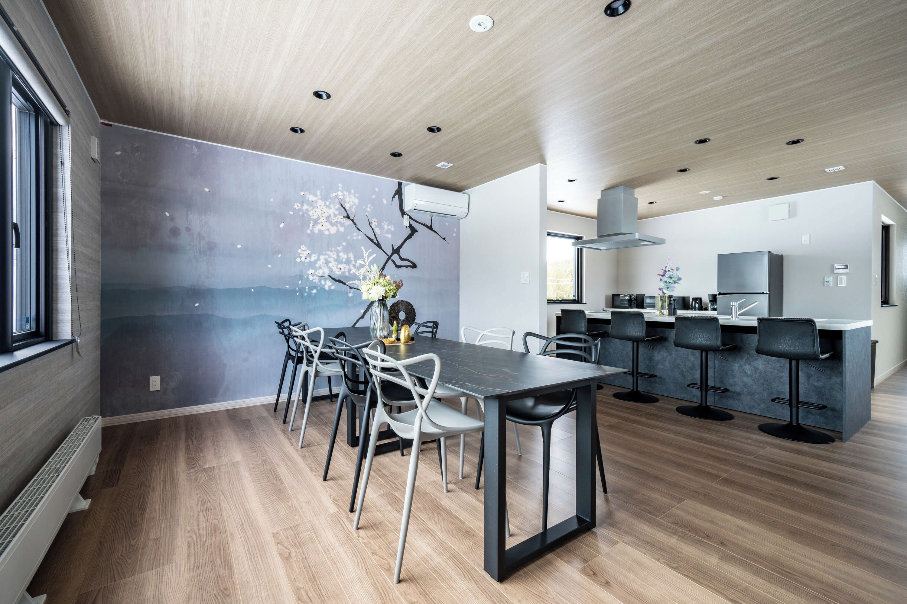 Una cocina moderna con una isla central, taburetes de bar y un comedor con una mesa larga y sillas.