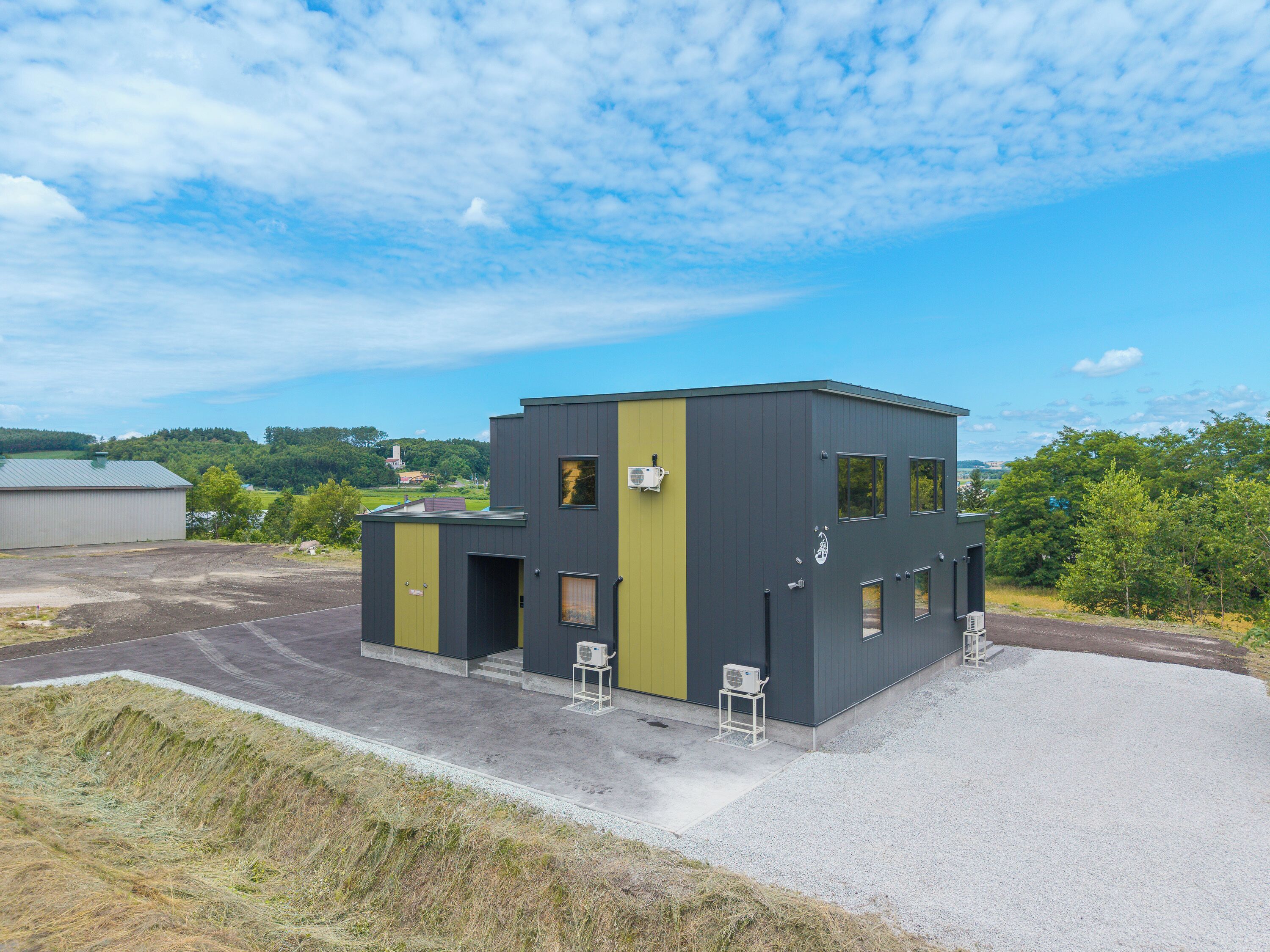 Un bâtiment moderne doté d’un toit plat, de deux portes apparentes et d’un petit espace extérieur avec un chemin de gravier.