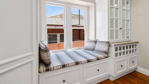 A built-in bench with storage drawers, a window with a view of a building, and a white cabinet with glass doors.