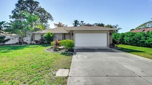 A single-story house with a garage, a front lawn, and a large tree. - Hot Tub & Outdoor Pool: Bonita Springs Getaway! (Bonita Springs)