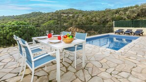 A poolside area with a table set for dining, surrounded by lounge chairs, and overlooking a lush landscape.