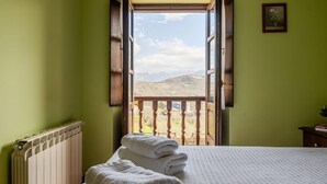 Ein Zimmer mit einem Bett, einem Heizkörper und einem offenen Fenster mit Blick auf einen Balkon und Berge.