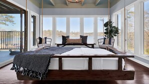 A bedroom with a large bed, a chandelier, and a view of the outdoors through large windows.