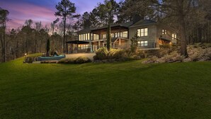 A modern two-story house with a large deck and a swimming pool, surrounded by a well-maintained lawn and trees.