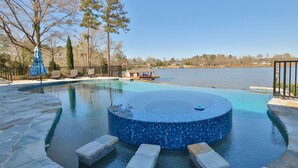 A swimming pool with a hot tub, stone steps, and a view of a lake.