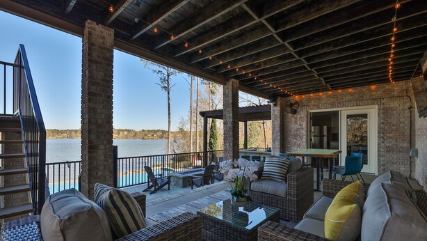 A covered outdoor seating area with wicker furniture, a glass table, and a view of a body of water.