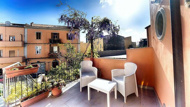 A balcony with two wicker chairs and a small table, surrounded by potted plants and a view of neighboring buildings. - Casa Zivula: A welcoming apartment situated at a short distance from the waterfront, with Free WI-FI. (Olbia)
