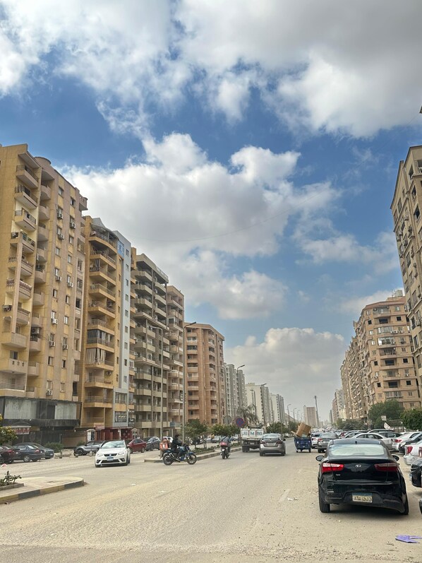 Une rue animée en plein centre-ville, bordée d’immeubles résidentiels à plusieurs étages, dotés de balcons et de climatiseurs.