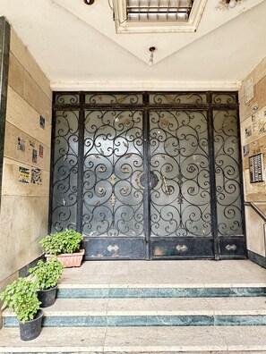 Une entrée d’immeuble agrémentée d’un portail en métal décoratif, de marches et de plantes en pot.