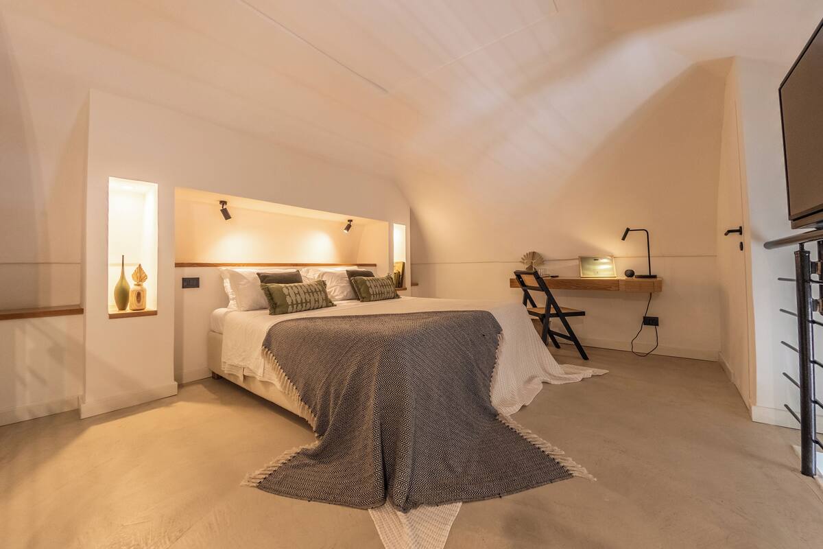 A bedroom with a bed, bedside table, lamp, and a TV.