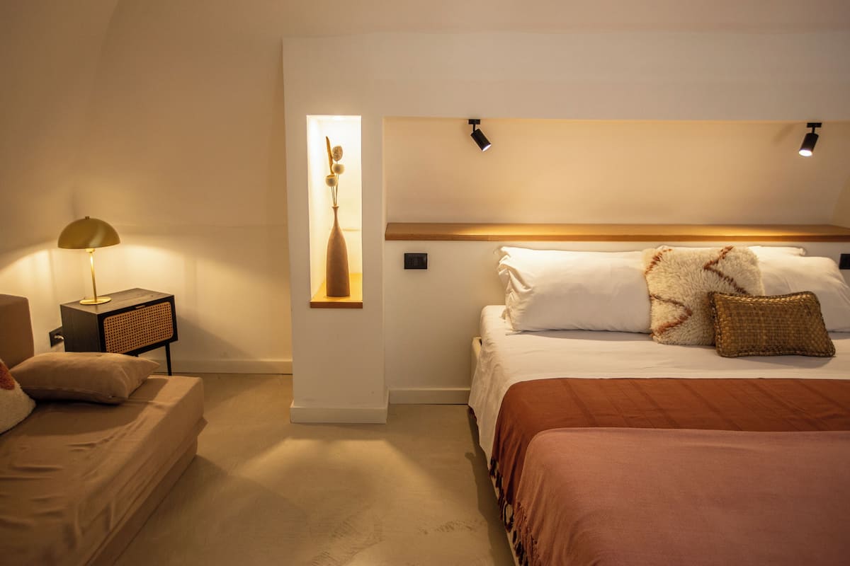 A bedroom with a bed, bedside table, lamp, and wall-mounted light fixture.