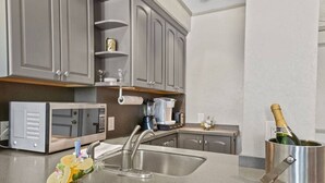Cocina moderna con armarios grises, un lavamanos de acero inoxidable, microondas, licuadora y una botella de champán.