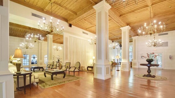 Un vestíbulo amplio con pisos de madera, columnas blancas y candelabros.
