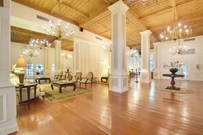 Un vestíbulo amplio con pisos de madera, columnas blancas y candelabros.