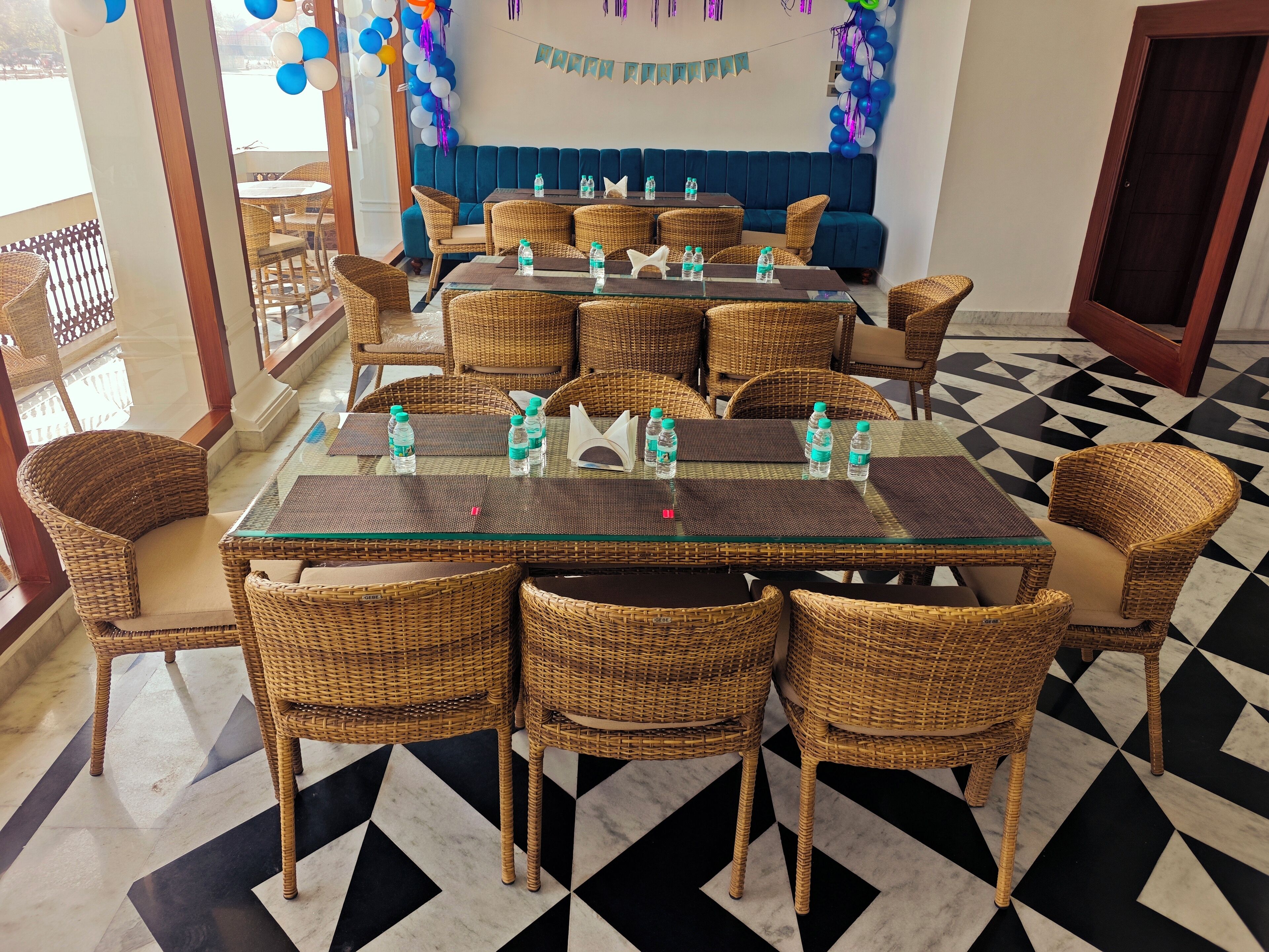 Un coin repas avec des chaises et des tables en osier, un canapé bleu et un sol à carreaux.