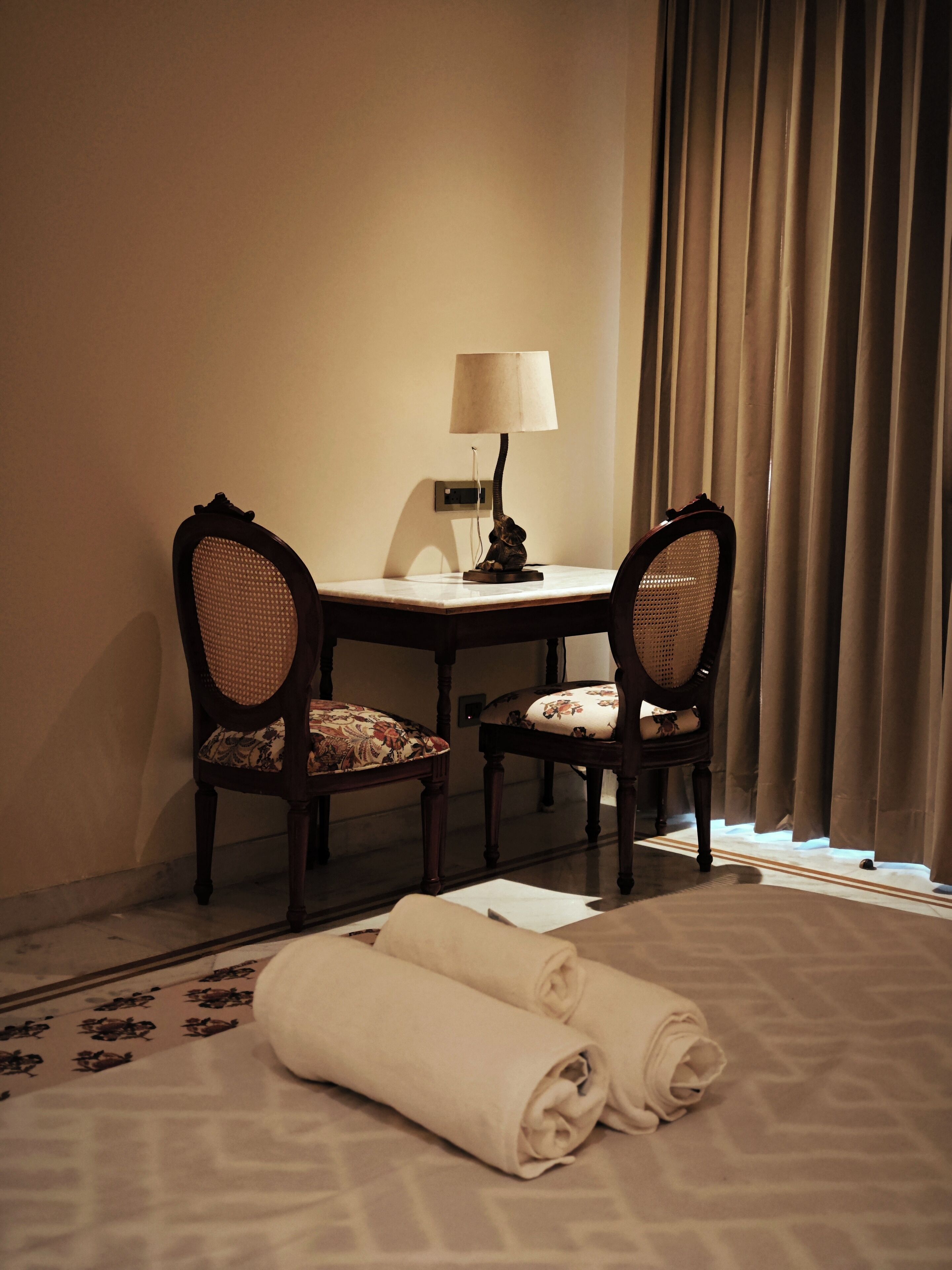 A hotel room with a bed, two chairs, a table, a lamp, and a window with curtains.
