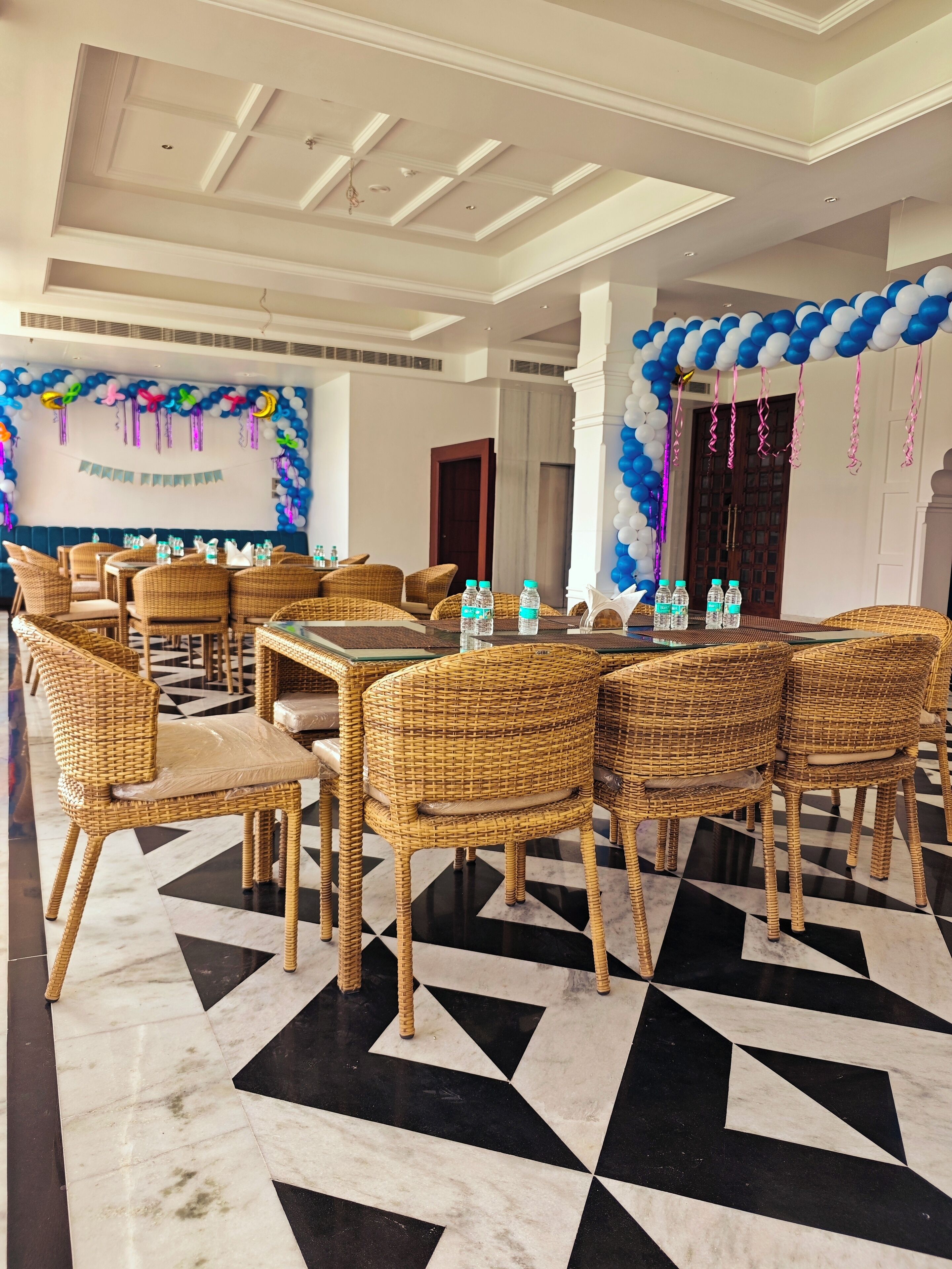 A room with a checkered floor, wicker chairs, and tables with water bottles.