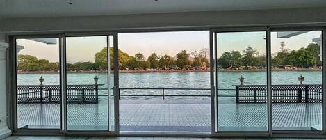 A spacious room with large floor-to-ceiling windows overlooking a water body, featuring a tiled floor and a metal railing.