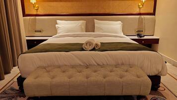 A hotel room with a large bed, two bedside tables, a headboard with a woven pattern, and a small bench at the foot of the bed.