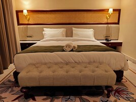 A hotel room with a large bed, two bedside tables, a headboard with a woven pattern, and a small bench at the foot of the bed.