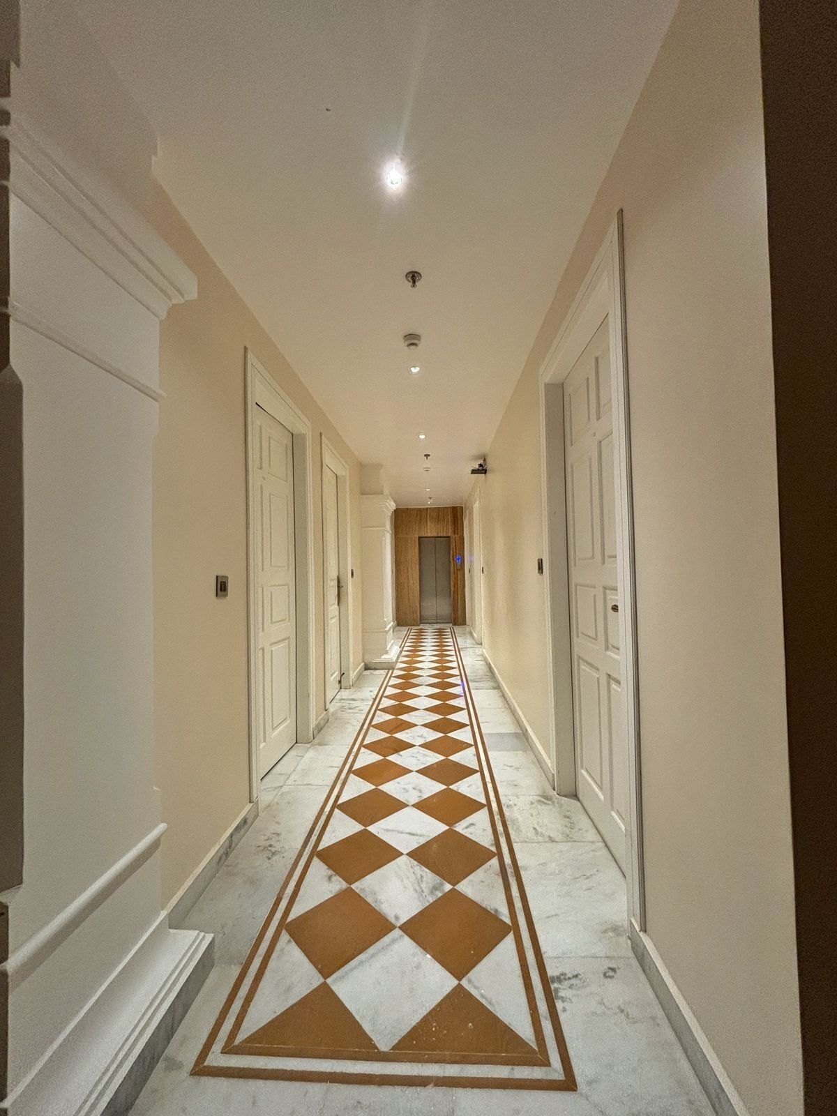Un couloir doté d’un sol à motifs à carreaux, de portes blanches et d’un éclairage encastré.