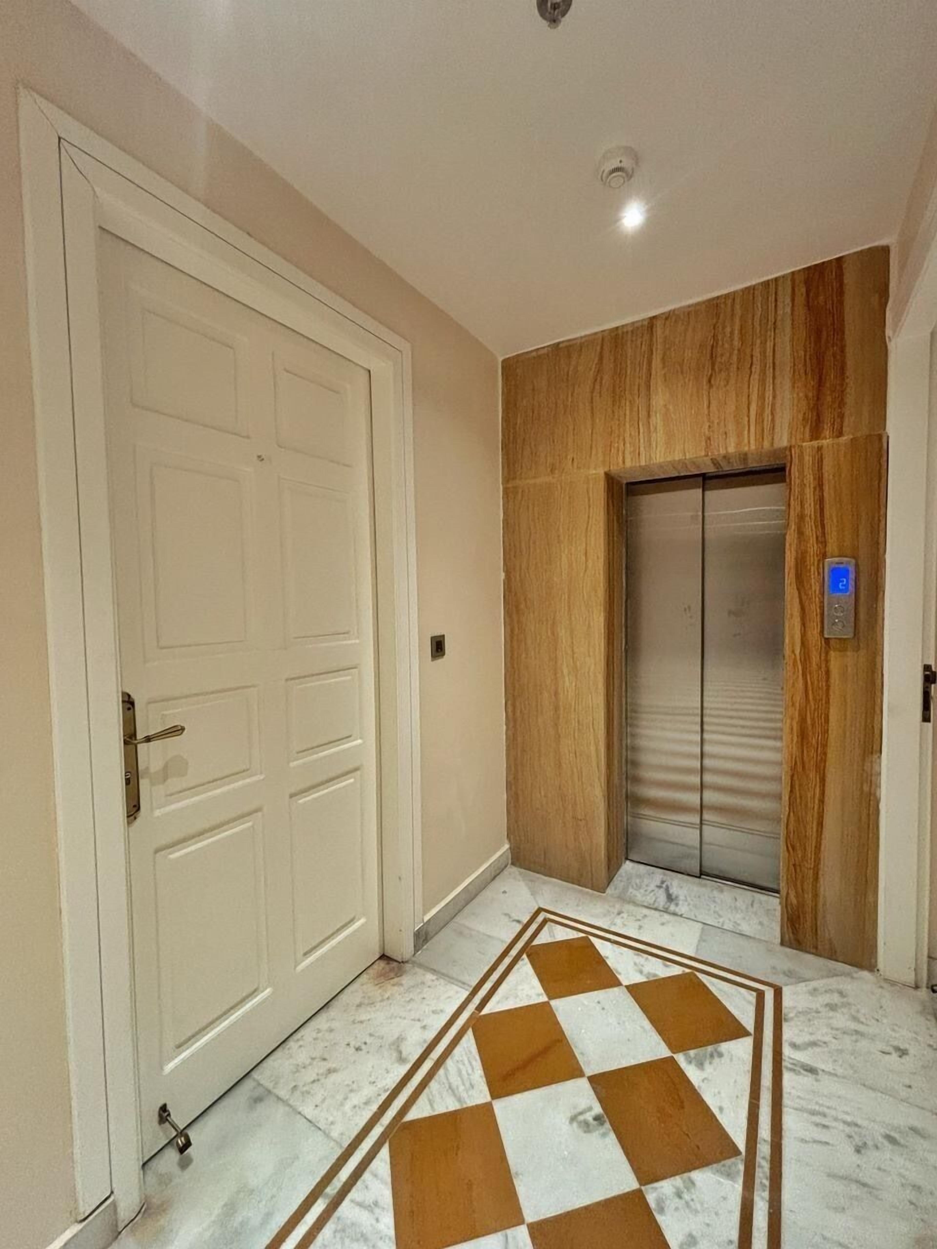 Um corredor com uma porta branca, um elevador e um chão estampado.
