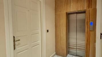 Um corredor com uma porta branca, um elevador e um chão estampado.